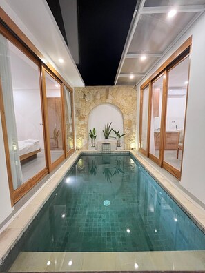 Piscina interna rettangolare con acqua cristallina, circondata da pareti con cornici in legno e dettagli in pietra.