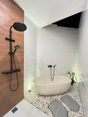 Ein modernes Badezimmer mit freistehender Badewanne, Duschkopf und einer kleinen Topfpflanze.