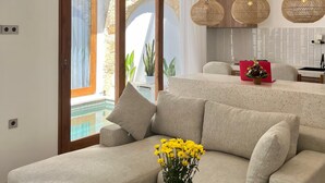 Ein modernes Wohnzimmer mit einer Couch, einem Couchtisch mit einer Vase voller gelber Blumen und einem Küchenbereich im Hintergrund.