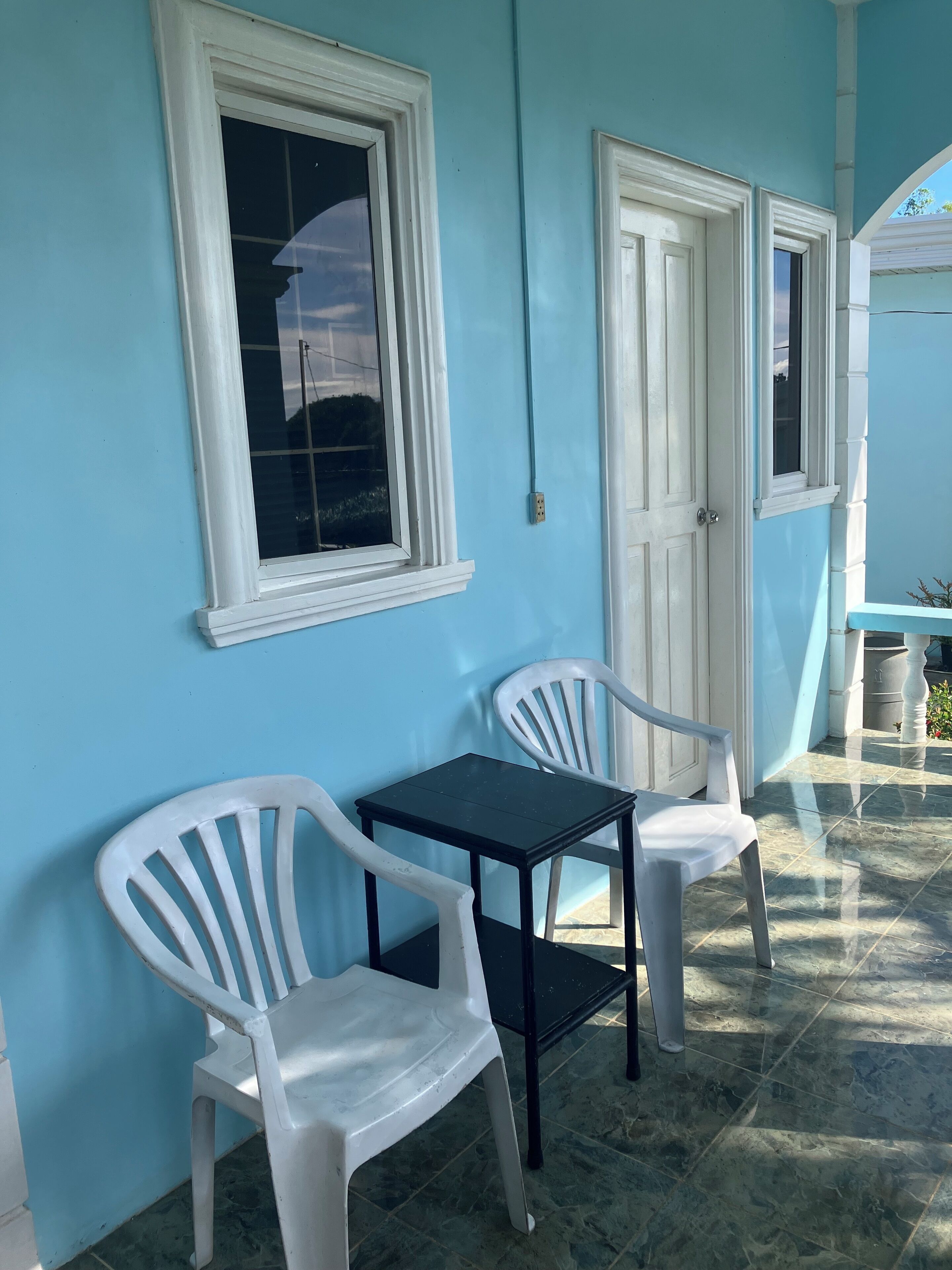 Een kamer met een blauwe wand, twee witte plastic stoelen, een klein zwart tafeltje en een deur.