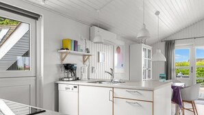 Une cuisine moderne avec des meubles blancs, un lave-vaisselle intégré et une machine à café. Une fenêtre offre une vue sur la verdure environnante.