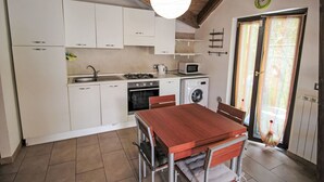 A compact kitchen with white cabinets, a wooden dining table, and a washing machine. - Il Covo Felice by Interhome (Gravellona Toce)