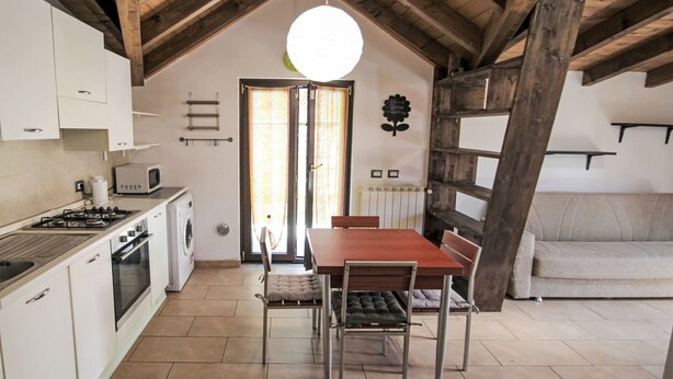 A kitchen with a dining table and chairs, a sofa, and a ceiling with exposed wooden beams. - Il Covo Felice by Interhome (Gravellona Toce)