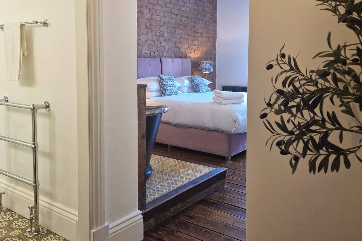 A bedroom with a brick wall, a bed with white bedding, and a wooden floor.