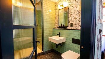 A bathroom with a glass shower enclosure, a white sink, and a toilet.