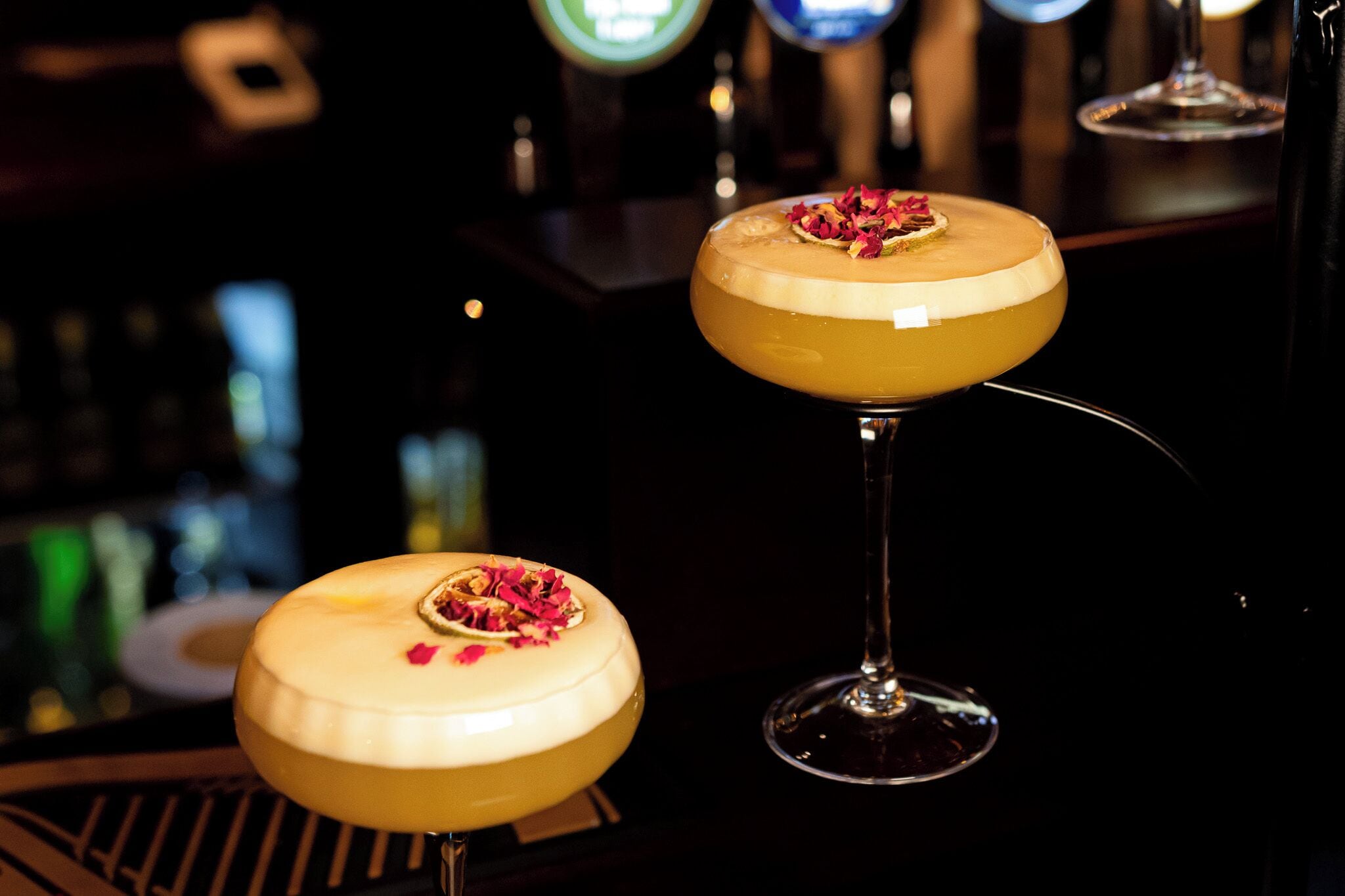 Two cocktail glasses with a creamy yellow drink and a garnish on a bar counter.
