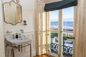 Un baño con un lavamanos blanco, un espejo y vista al mar a través de una puerta de cristal.
