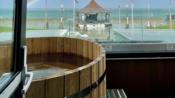 Un jacuzzi de madera con vista a una playa y un arcoíris.