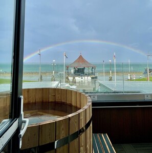 Ein hölzernes Whirlpool mit Blick auf einen Strand und einen Regenbogen.