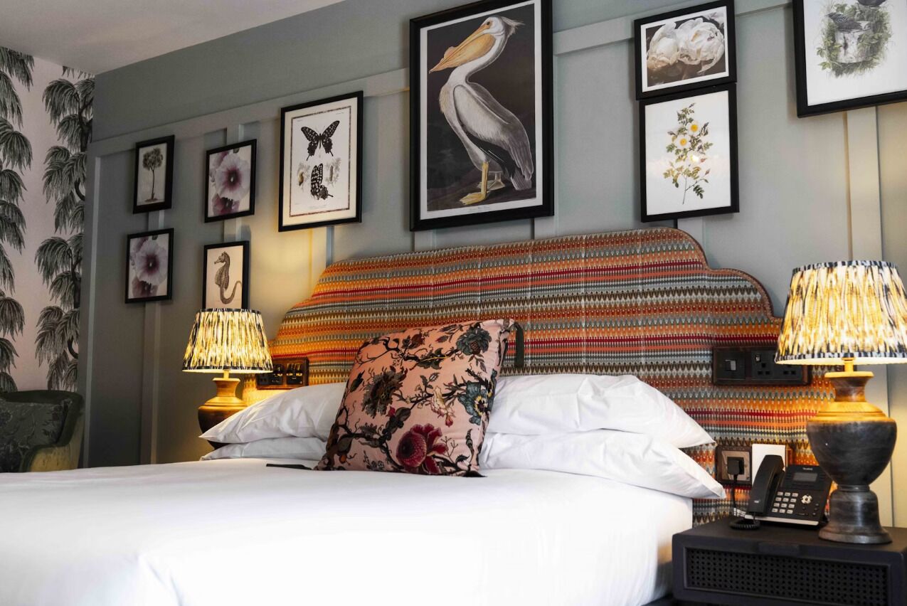 A neatly made bed with a floral pillow, two bedside lamps, and framed artwork on the wall.
