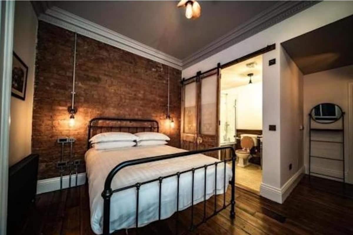 A bedroom with a brick wall, a bed with a metal frame, and a wooden floor.