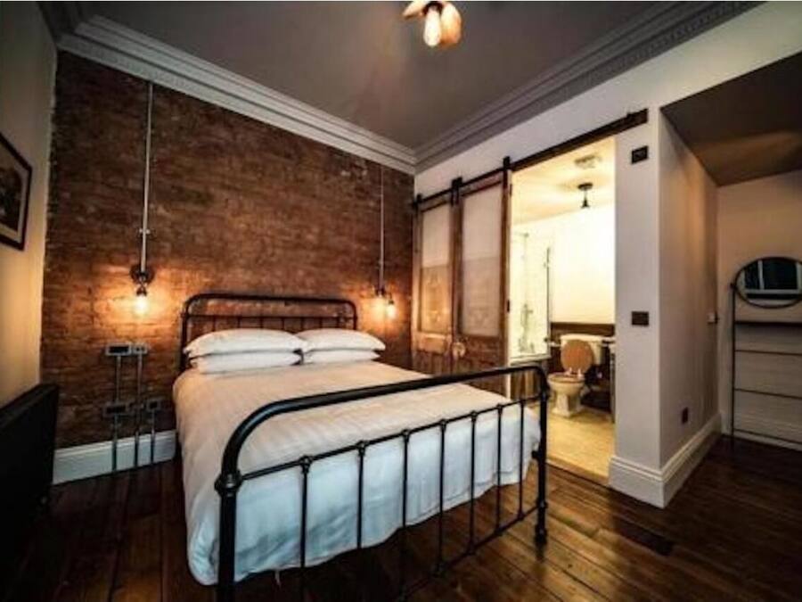 A bedroom with a brick wall, a bed with a metal frame, and a wooden floor.