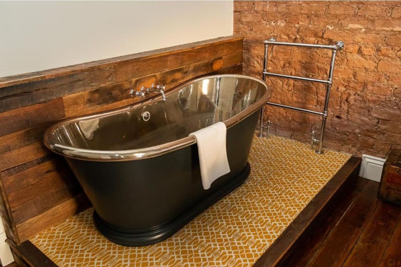 A bathtub in a room with wooden flooring and a brick wall.