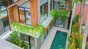 A modern building with a glass balcony, a small pool, and lush greenery. - Nanna Villa Unit 4 by Betterplace (Canggu)