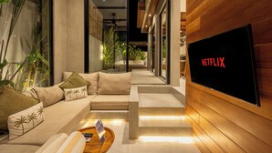 A modern living room with a sofa, coffee table, and a large flat-screen TV displaying the Netflix logo. - Nanna Villa Unit 4 by Betterplace (Canggu)