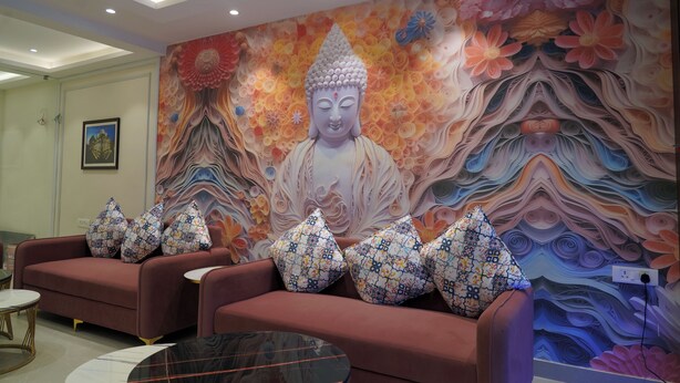 Ein Zimmer mit Buddha-Wandgemälde, roten Sofas, gemusterten Kissen und einem runden Tisch.
