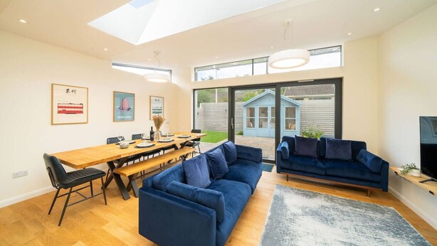 Ein modernes Wohnzimmer mit einem Holzesstisch, blauen Sofas und einem großen Fenster mit Blick auf einen Garten.