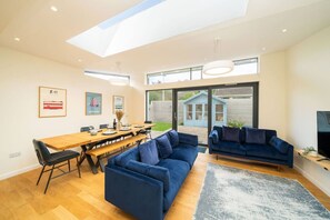 Ein modernes Wohnzimmer mit einem Holzesstisch, blauen Sofas und einem großen Fenster mit Blick auf einen Garten.