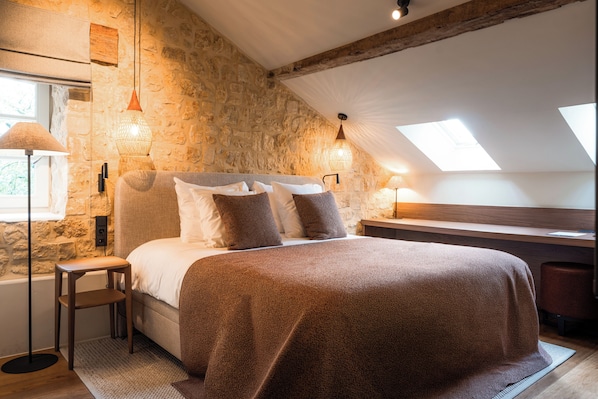 A bedroom with a stone wall, a bed with a brown blanket, two bedside lamps, and a skylight. - Van Oys Maastricht Retreat, a Leading Hotel of the World (Eijsden)