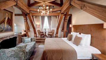 A bedroom with a large bed, a wooden ceiling, a painting on the wall, and a fireplace.