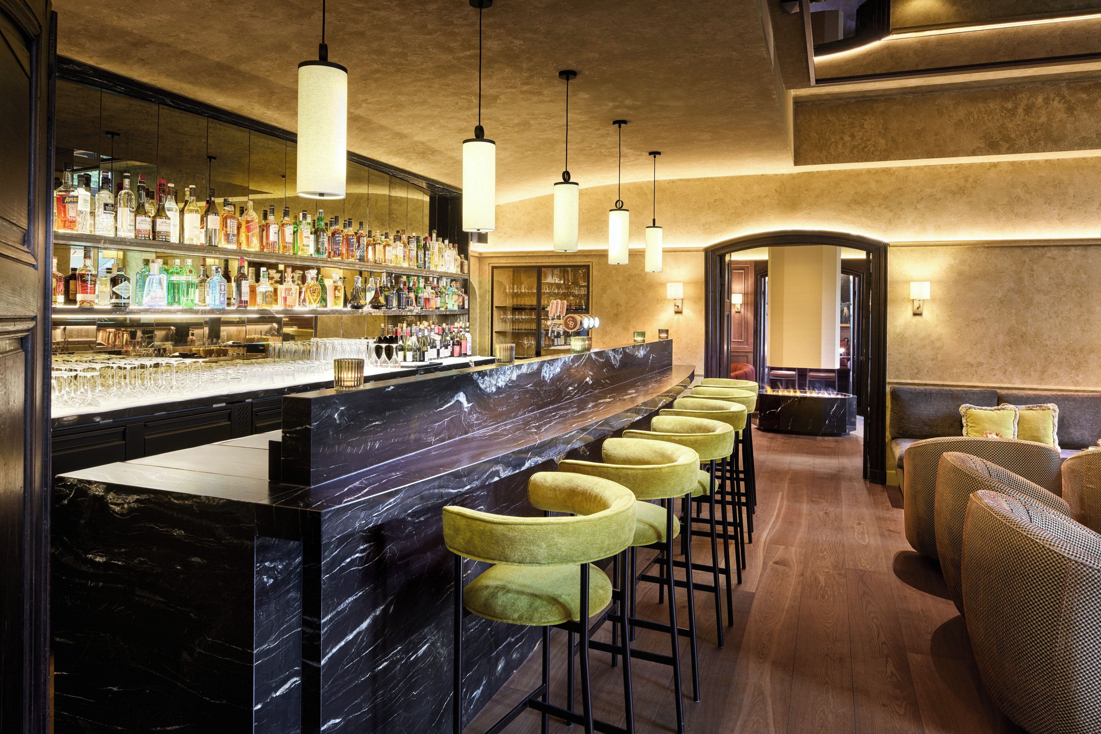 Zona de bar con mostrador de mármol, varios taburetes y una variedad de botellas.
