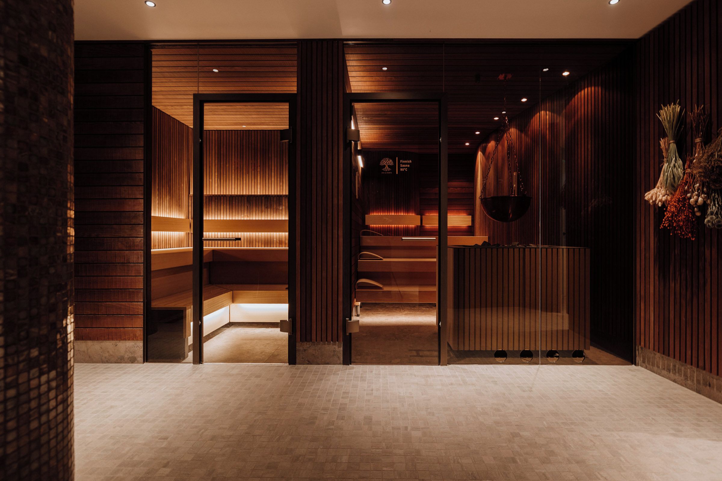 Un interior moderno con paneles de madera, una recepción y un cartel de sauna que indica 90°C.