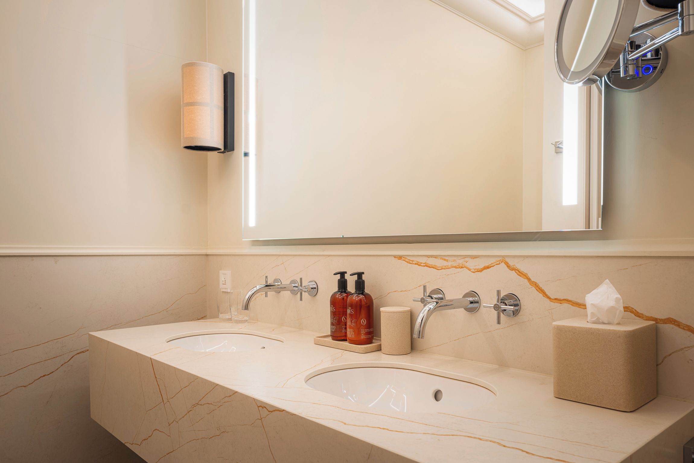 A bathroom with two sinks, a mirror, a towel dispenser, and a soap dispenser.