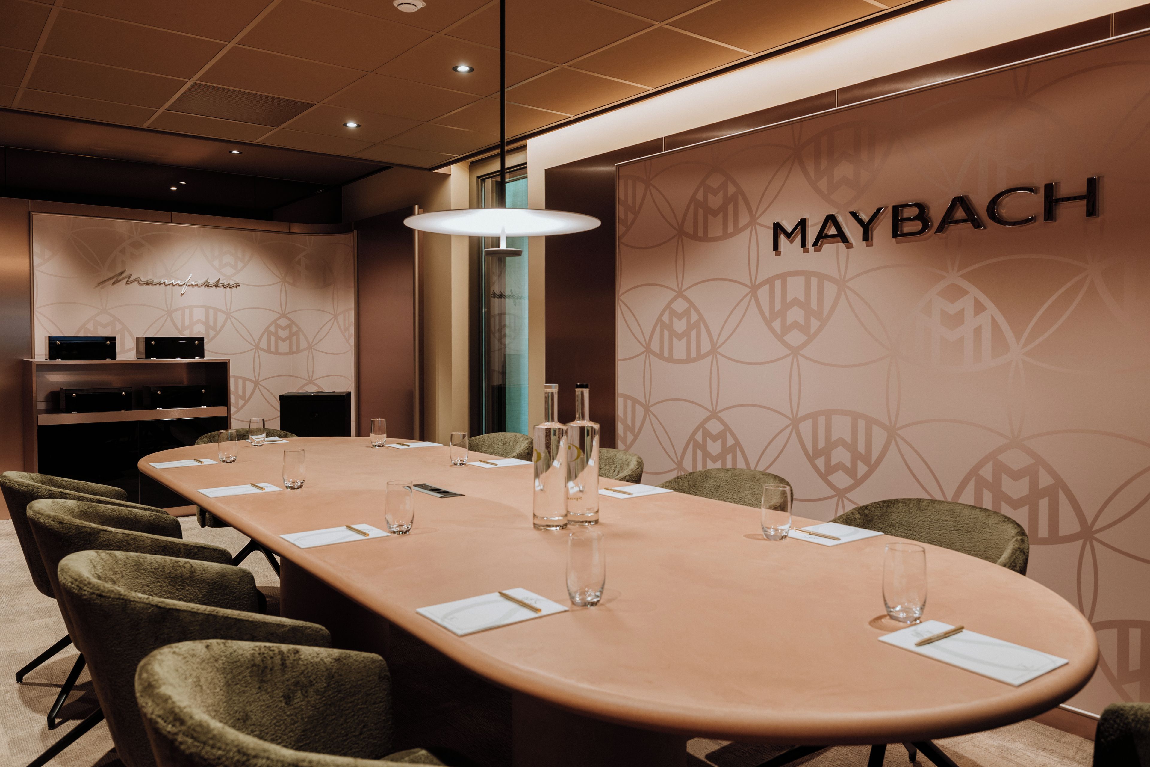 Een vergaderzaal met een lange tafel, stoelen en een muur met het Maybach logo.