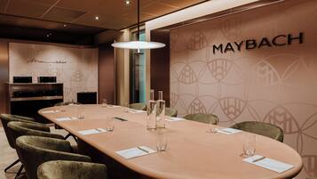 Een vergaderzaal met een lange tafel, stoelen en een muur met het Maybach logo.