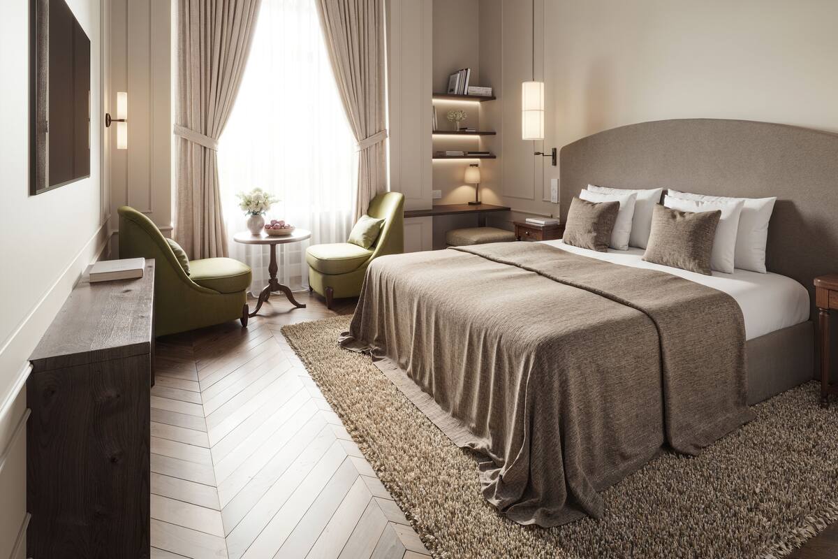 Une chambre d’hôtel avec un grand lit, un bureau, une chaise, une petite table avec un vase et une bibliothèque.
