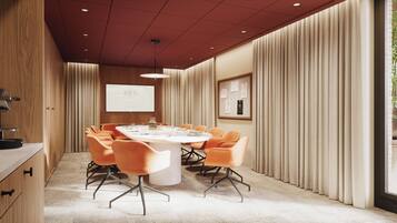 A conference room with a round table, orange chairs, a projector screen, and a framed certificate on the wall.