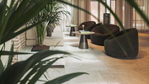 Un hall d’entrée moderne avec un banc en pierre, deux tables rondes ornées de livres et une grande plante en pot.