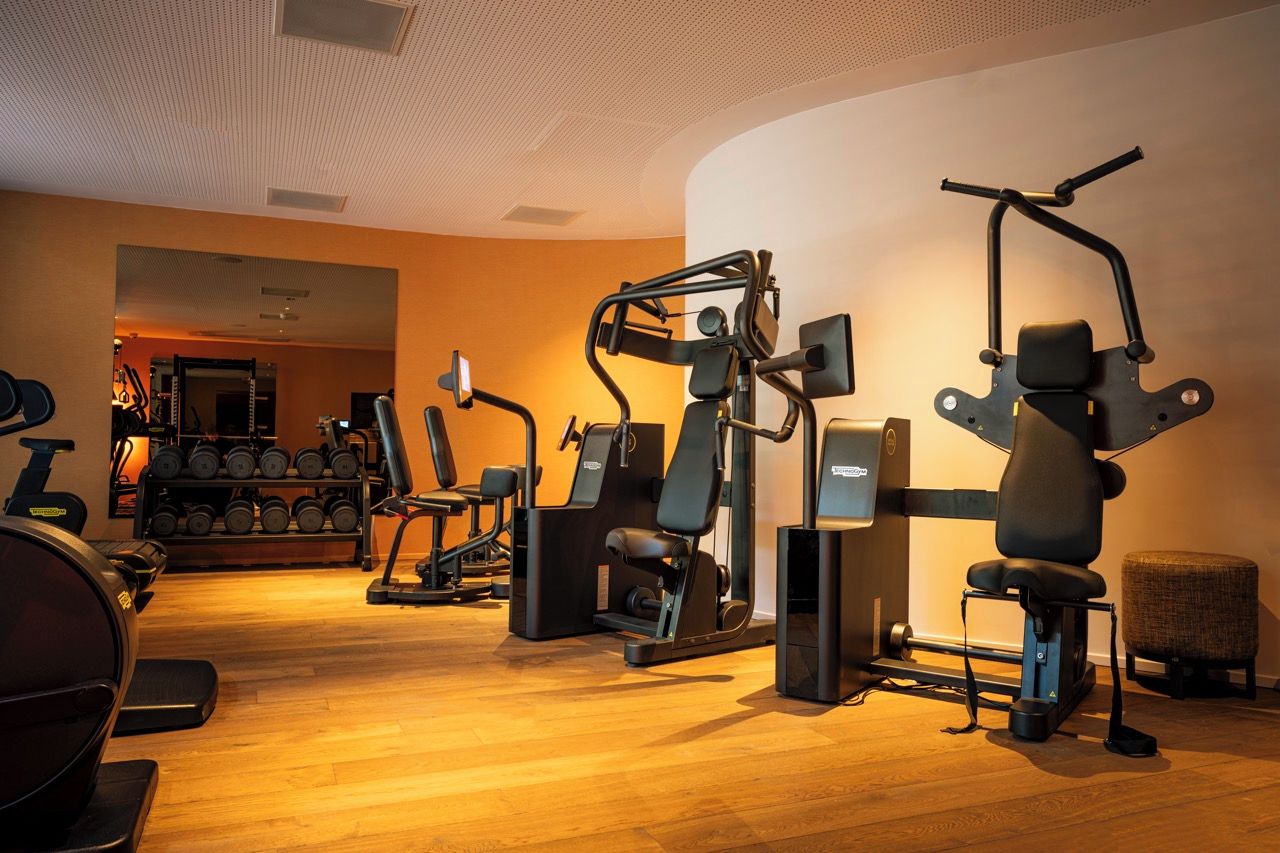 Ein Fitnessstudio mit verschiedenen Trainingsgeräten, darunter Laufbänder, Kraftgeräte und Kurzhanteln.