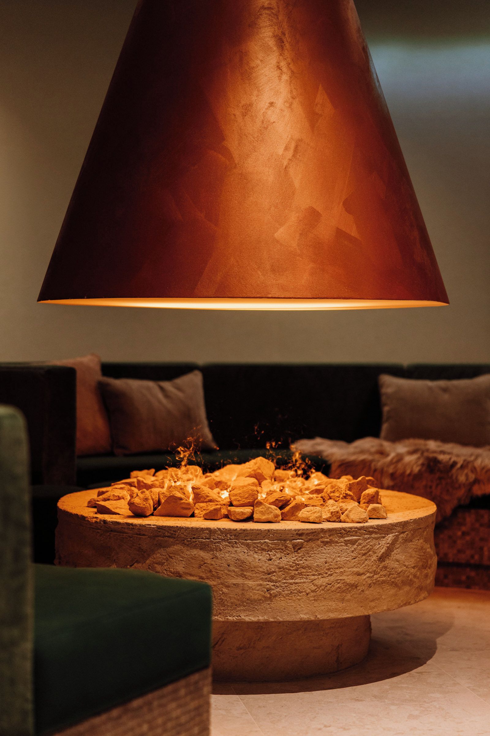 Una habitación con una chimenea de piedra, un sofá verde y un sillón oscuro.