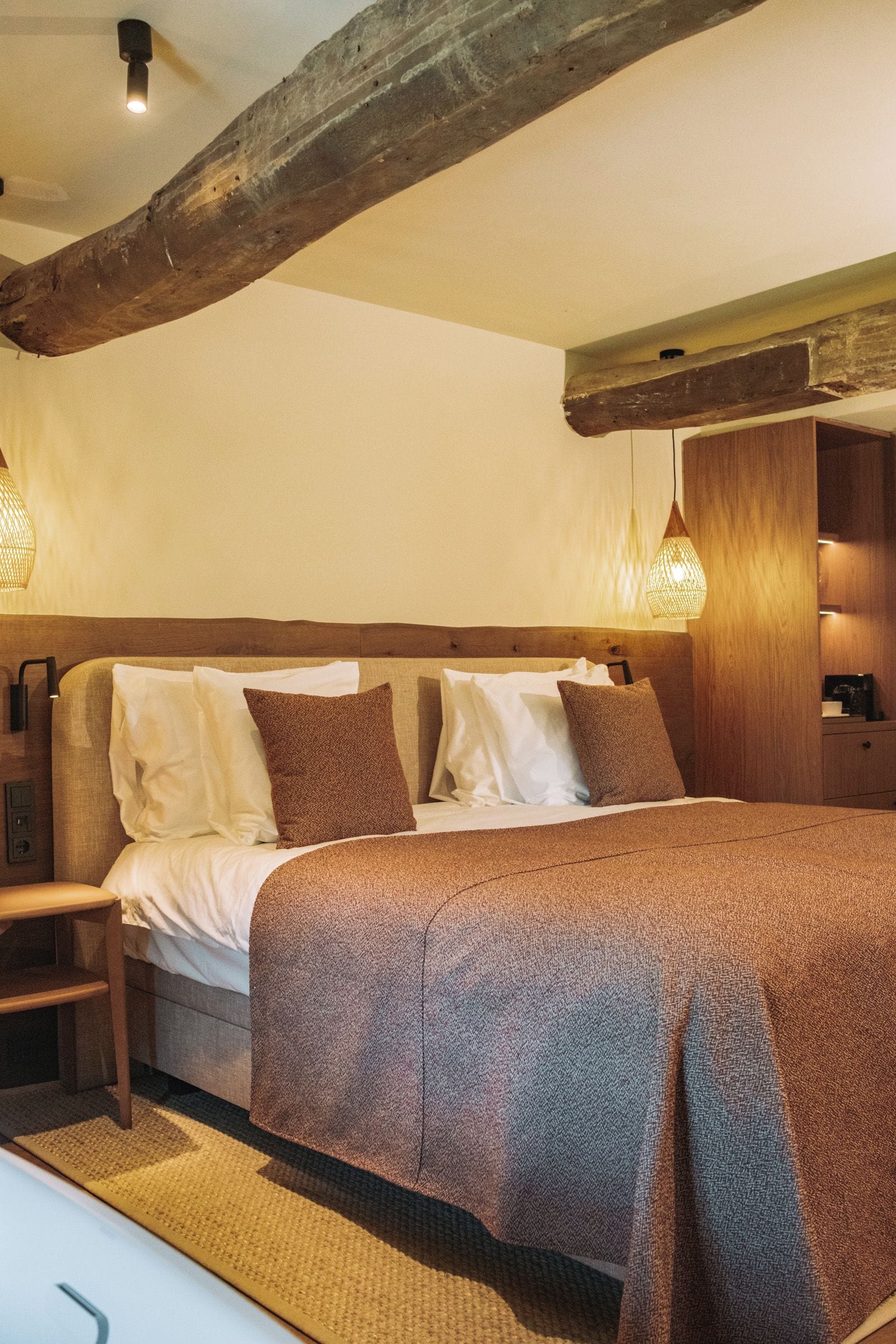 Een slaapkamer met een houten hoofdbord, een bed met een gebreid plaid, twee bedlampjes en een nachtkastje van hout.