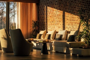 A modern living room with a brick wall, a sofa set, a coffee table, and a large window with curtains. - Van Oys Maastricht Retreat, a Leading Hotel of the World (Eijsden)