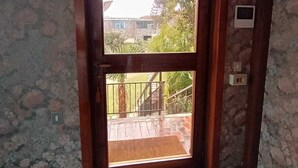 Um quarto com porta de madeira que dá para uma varanda com vista para uma casa e vegetação.