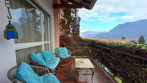 Varanda com móveis de vime e uma mesa, com vista para uma paisagem montanhosa.