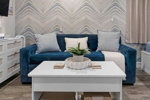 Un salon moderne avec un canapé bleu, une table basse blanche et un mur orné d’un motif.