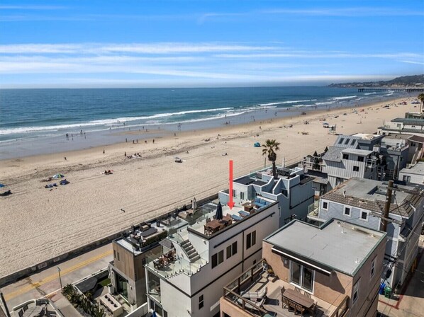 Un hôtel situé en bord de mer, doté d’une terrasse sur le toit, offrant une vue sur la plage et sur une jetée visible au loin.