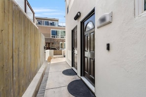 A narrow pathway leading to a building with a wooden fence on one side and a black door on the other.