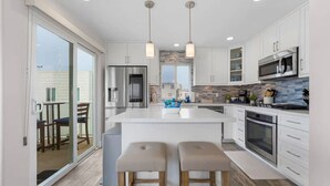 A modern kitchen with a large island, stainless steel appliances, and a sliding glass door leading to a balcony. - Panoramic Ocean View Huge Rooftop Deck - Sleeps 8 (San Diego)