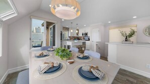 A modern kitchen with white cabinets, a central island, and a dining area with a table set for four. - Panoramic Ocean View Huge Rooftop Deck - Sleeps 8 (San Diego)