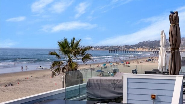 A beach view from a balcony with a palm tree, beach umbrellas, and a pier in the distance. - Panoramic Ocean View Huge Rooftop Deck - Sleeps 8 (San Diego)