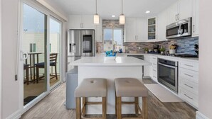 A modern kitchen with a central island, stainless steel appliances, and a view to an outdoor area. - Stunning Ocean Views Rooftop Deck - Sleeps 10 (San Diego)