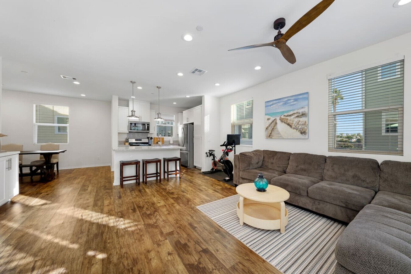 A spacious living area with a large gray sofa, a wooden coffee table, and a kitchen with white cabinets and a central island.