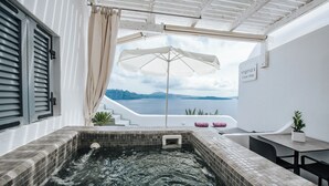 A hot tub with a view of the sea, a white wall with a sign, and a table with a plant.