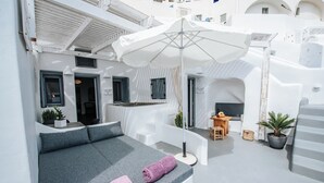 A modern, white-walled room with a grey sofa, two pink towels, a wooden table, and a potted plant.