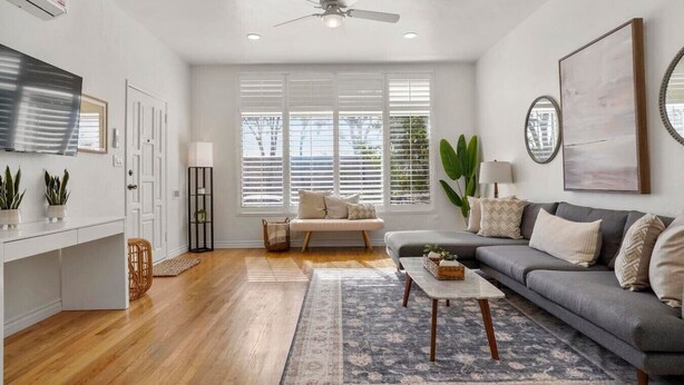 A modern living room with a grey sofa, a coffee table, a TV, and a ceiling fan.