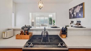 A modern kitchen with a gas stove, a toaster, and a window with blinds.